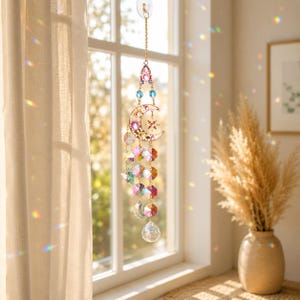 Può includere: Un acchiappasole in metallo dorato con una cornice a forma di mezzaluna e stella, decorato con cristalli di vetro sfaccettati multicolori. L'ornamento pende da una catenina sottile e include vari cristalli pendenti.