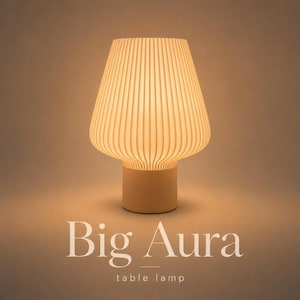 May include: A table lamp with a cylindrical base and a wide, fluted, bell-shaped shade that emits a warm, soft glow. The text Big Aura table lamp is printed in white at the bottom of the image, centred below the illuminated lamp fixture.