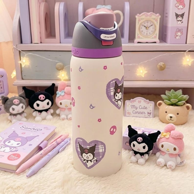 Puede incluir: Una botella de agua de color crema con una tapa morada que tiene un mecanismo de bloqueo con la etiqueta "Lift to Unlock". La botella est&aacute; decorada con peque&ntilde;os iconos de calaveras moradas y rosas, flores diminutas y dos grandes corazones de cuadros morados con el personaje Kuromi.