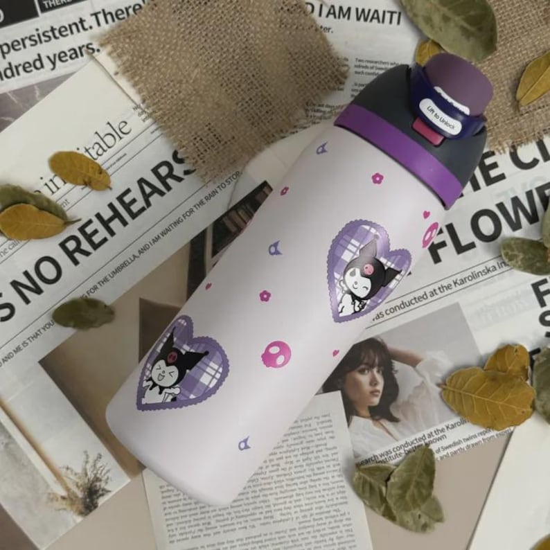 Puede incluir: Una botella de agua blanca con tapa morada y un mecanismo de apertura con la etiqueta "Lift to Unlock". La botella presenta un patr&oacute;n repetitivo de peque&ntilde;as flores rosas, calaveras rosas y dos pegatinas moradas en forma de coraz&oacute;n.