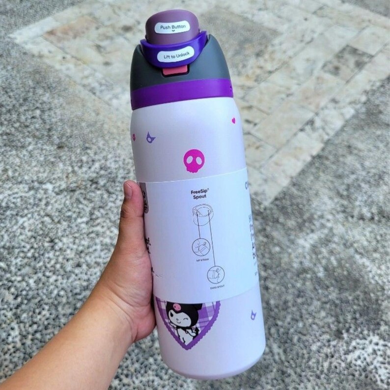 Puede incluir: Una botella de agua de color morado claro con una tapa morada oscura que incluye un bot&oacute;n y un mecanismo de desbloqueo. La etiqueta blanca muestra el texto FreeSip Spout con diagramas, un icono de calavera rosa y un gr&aacute;fico de personaje.