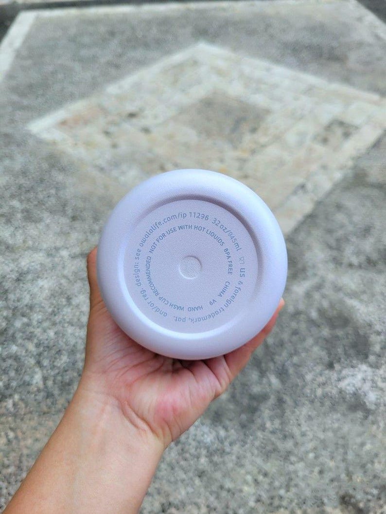 Puede incluir: La base circular de una botella de agua color lavanda claro con texto impreso que incluye 32oz/945ml, libre de BPA y no apto para l&iacute;quidos calientes. El texto tambi&eacute;n indica owalalife.com/ip 11296, se recomienda lavar a mano y fabricado en China.