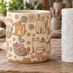 May include: A cream-colored ceramic mug featuring embossed, hand-painted illustrations of various cats, hearts, stars, and small gifts, positioned next to a white cylindrical clay texture roller with matching cat and heart patterns.