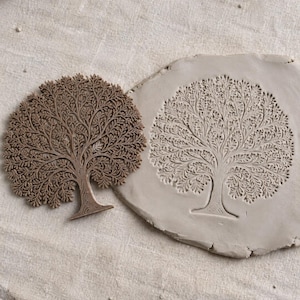 May include: A brown tree-shaped stamp with intricate branch and leaf details positioned next to a circular piece of light grey clay that features an identical tree impression pressed into its surface, showcasing the stamp's design capabilities.