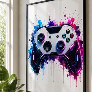 May include: Framed art print featuring a white and black video game controller design. The controller is accented with neon blue, purple, and pink lights, set against a backdrop of colorful paint splatters. The print is in a black frame.