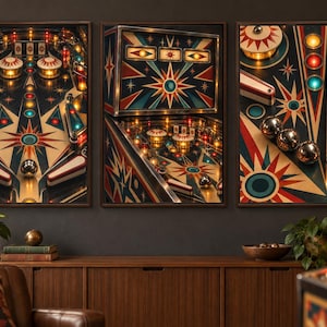 May include: A triptych of wall art prints featuring a vintage pinball machine with a dark blue, red, and cream starburst graphic design. The artwork displays illuminated bumpers, metallic silver balls, and a spring-loaded plunger mechanism.