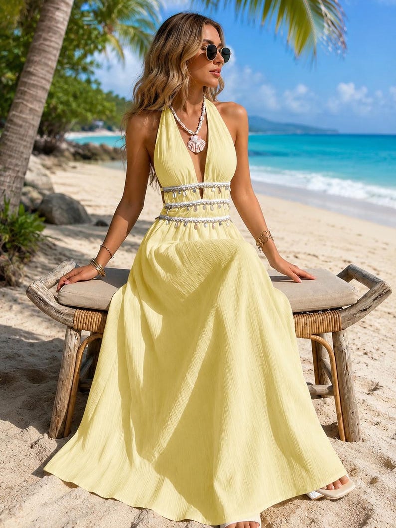 Puede incluir: Un vestido largo de color amarillo p&aacute;lido con un escote en V profundo, un corpi&ntilde;o estilo halter y una cintura con aberturas. La cintura est&aacute; acentuada con dos filas horizontales de flecos de cuentas blancas y plateadas sobre la falda.