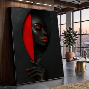 May include: A framed art print depicting a person with dark skin, red lips, and red eye makeup. The artwork has a black and red colour scheme, with a red accent on the side. The person's hand with red nails is visible.