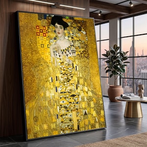 May include: A framed print of a Gustav Klimt painting, featuring a woman in a golden dress with intricate patterns. The artwork has a gold background with geometric shapes and floral motifs. The woman has a black hat and red lipstick.