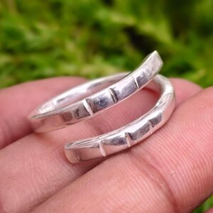 May include: A silver bypass ring featuring a polished metallic finish and a series of evenly spaced vertical notches carved along the outer surface of the band. The ring has an open, overlapping design that curves around the finger.