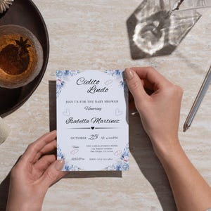 Peut inclure: Une invitation à une baby shower avec le texte "Cielito Lindo" et "Isabella Martinez". L'invitation a un fond bleu clair avec des accents floraux. La date est le 25 octobre à 16h00.