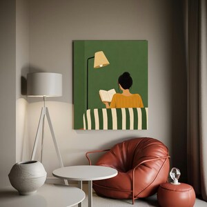 Puede incluir: Una impresión artística representa a una persona leyendo un libro, sentada en un sofá a rayas, bajo una lámpara. La obra de arte está montada sobre un fondo verde. Una silla de cuero roja y mesas auxiliares blancas están en primer plano.