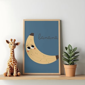 Puede incluir: Una lámina enmarcada con una banana de color amarillo claro con cara sonriente, tallo y punta de color marrón oscuro, y la palabra banana escrita en cursiva sobre un fondo azul sólido, junto a un peluche de jirafa y una planta.