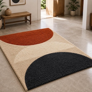 Peut inclure: Un tapis rectangulaire à poils longs présentant une surface texturée avec un motif géométrique. Le design se compose d'un grand demi-cercle orange brûlé en haut, d'un demi-cercle noir en bas et d'un fond beige sur l'ensemble.