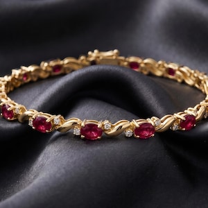 Puede incluir: Una pulsera de oro con una serie de rubíes rojos de corte ovalado que se alternan con pequeños diamantes blancos redondos. Los eslabones metálicos entre las piedras preciosas tienen un diseño curvo en forma de S y un cierre de seguridad.