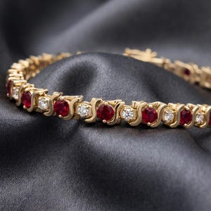 Può includere: Un bracciale tennis in oro con un'alternanza di rubini rossi e diamanti bianchi a taglio rotondo. Le pietre sono incastonate in un design a maglie metalliche a forma di S che collega ogni gemma, creando una fascia circolare continua.
