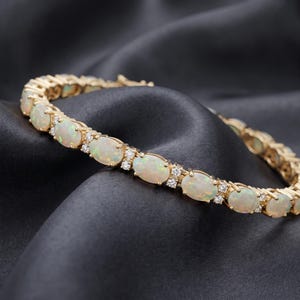 May include: A gold tennis bracelet featuring a series of oval-shaped, iridescent opals alternating with small, clear, round-cut diamonds. The bracelet is constructed with individual metal links that hold each gemstone securely in a prong setting.