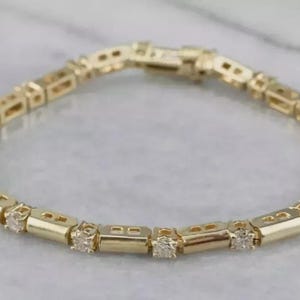 Puede incluir: Una pulsera de eslabones dorados con segmentos rectangulares de oro pulido que alternan con piedras redondas, claras y facetadas engastadas en oro. La pulsera cuenta con un mecanismo de cierre seguro y un diseño circular continuo.