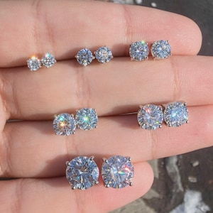 May include: Three pairs of round-cut stud earrings with clear, faceted stones set in silver-toned metal prongs. The earrings are arranged in descending order of size, showcasing a brilliant sparkle and reflective quality on each stone surface.