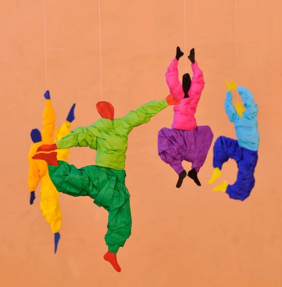 Handmade paper dancer figures suspended in a colorful kinetic mobile that sways and balances with the air — the 'a real person made this' feeling in full effect.