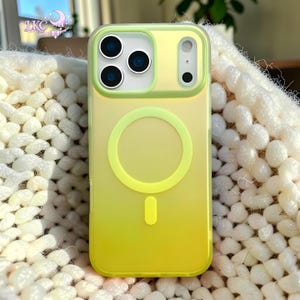 Puede incluir: Una funda para smartphone con un degradado en amarillo y verde lima. La funda presenta un anillo magn&eacute;tico MagSafe circular y un im&aacute;n de alineaci&oacute;n vertical en el centro. El &aacute;rea de la c&aacute;mara est&aacute; elevada con tres aberturas circulares.