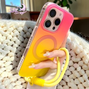 Puede incluir: Una funda para smartphone con un degradado vibrante que va desde el rosa intenso en la parte superior hasta el amarillo brillante en la inferior. Incluye un anillo de carga magn&eacute;tico circular en la parte posterior y una correa amarilla.