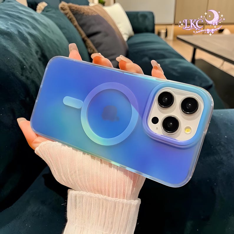 Puede incluir: Una funda rectangular para smartphone con un acabado iridiscente en degradado azul y morado. La parte trasera presenta un anillo de carga magn&eacute;tico circular y un im&aacute;n de alineaci&oacute;n ovalado. El m&oacute;dulo de c&aacute;mara est&aacute; elevado con tres aberturas.