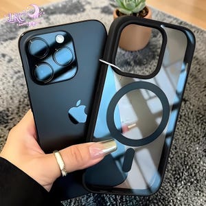 May include: A matte black smartphone with a triple-lens camera system and an Apple logo, paired with a matching black transparent protective phone case featuring a circular magnetic charging ring and a vertical alignment magnet on the back.