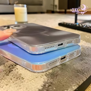 Puede incluir: Dos fundas transparentes para smartphone apiladas una sobre otra. La funda superior es transparente con un dise&ntilde;o de anillo magn&eacute;tico circular, mientras que la inferior presenta un panel trasero azul s&oacute;lido. Ambas tienen recortes precisos.
