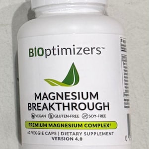 May include: A white bottle of "Magnesium Breakthrough" dietary supplement. The label includes the brand name "BioOptimizers", a green leaf logo, and text indicating it is vegan, gluten-free, and soy-free. The bottle contains 60 veggie caps.