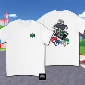 Può includere: Una t-shirt bianca con un piccolo logo N64 colorato sul petto e una grafica a vista esplosa sul retro che mostra una console di gioco smontata, una scheda elettronica, una cartuccia di gioco e quattro controller in rosso, blu, grigio e verde.