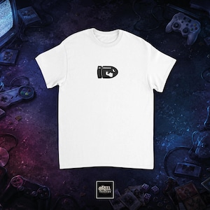 Peut inclure: T-shirt blanc avec un motif de balle noir. L'image est centrée, entourée de consoles de jeux rétro, de manettes et de cartouches de jeux. Le fond est sombre et texturé, avec des teintes violettes et bleues.