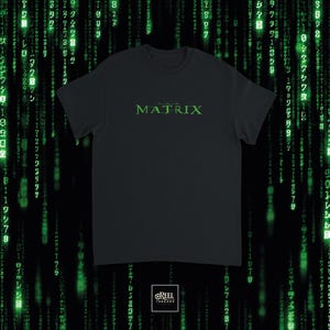 Könnte beinhalten: Ein schwarzes T-Shirt mit kurzen Ärmeln und dem Wort MATRIX, das in einer stilisierten grünen Schrift auf der Brust gedruckt ist. Das Design ist mittig auf dem Kleidungsstück platziert, das einen Rundhalsausschnitt und eine Standardpassform hat.