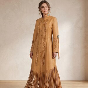 May include: A tan leather duster coat featuring a high collar, a front button closure, and vertical leather lacing details along the chest. The sleeves and hem are adorned with long leather fringe, and the collar and sleeves feature turquoise stone accents.