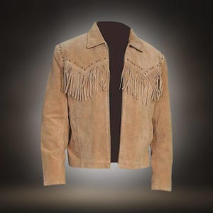 May include: A tan suede jacket featuring long fringe detailing across the chest and back yoke. The jacket includes a classic collar, long sleeves, and a front opening. The suede material has a soft, matte texture with visible stitching along the seams.