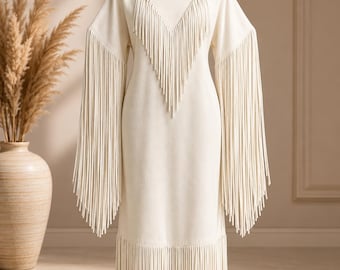 May include: A cream-colored long-sleeve dress featuring extensive fringe detailing. The fringe is arranged in a V-shape across the chest, along the full length of the sleeves, and around the bottom hem of the garment. The dress has a round neckline.