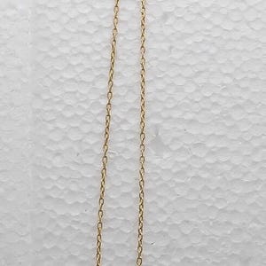 May include: A gold-tone necklace featuring a delicate chain and a single letter I pendant. Attached to the clasp is a rectangular tag with the text Jewels by TRIFARI MADE IN U.S.A. The necklace is suspended vertically against a textured white surface.