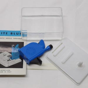 May include: An Elite Blue automatic needle threader kit. The kit includes a blue plastic threader, a white plastic tray, a clear plastic case, and an instruction booklet. The booklet has the text "Elite Blue" and "Made in Italy".