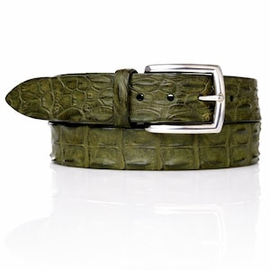 May include: A green leather belt with a crocodile skin effect. The belt features a silver-coloured rectangular buckle. The belt is shown against a white backdrop.