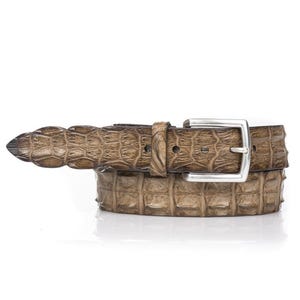 Op de afbeelding: Een bruine leren riem met een textuur die op krokodillenleer lijkt. De riem heeft een zilverkleurige vierkante gesp en een bijpassende lus. De riem heeft een neutrale kleur en lijkt van hoogwaardig leer te zijn.