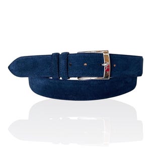 Peut inclure: Une ceinture en daim bleu marine avec une boucle argentée. La ceinture est faite d'un matériau doux et texturé et présente un design classique. La boucle est rectangulaire et a une finition polie. C'est un accessoire élégant.