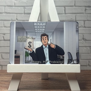 May include: A rectangular credit card skin featuring a cartoon illustration of a person in a suit holding a money bag with a dollar sign. The background depicts an office hallway. The text Mo' Money, Mo' Problems is printed at the bottom.