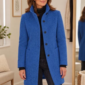 May include: A vibrant blue, knee-length coat featuring a structured collar, long sleeves with ribbed black cuffs, and a front button closure. The coat is crafted from a textured fabric and includes two large, deep patch pockets on the front panels.