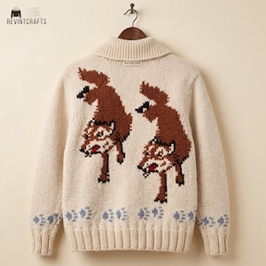 May include: A cream-colored knit cardigan featuring a shawl collar and long sleeves. The back displays two brown wolf motifs with white and black details, positioned above a row of light blue paw prints along the ribbed hem and sleeve cuffs.