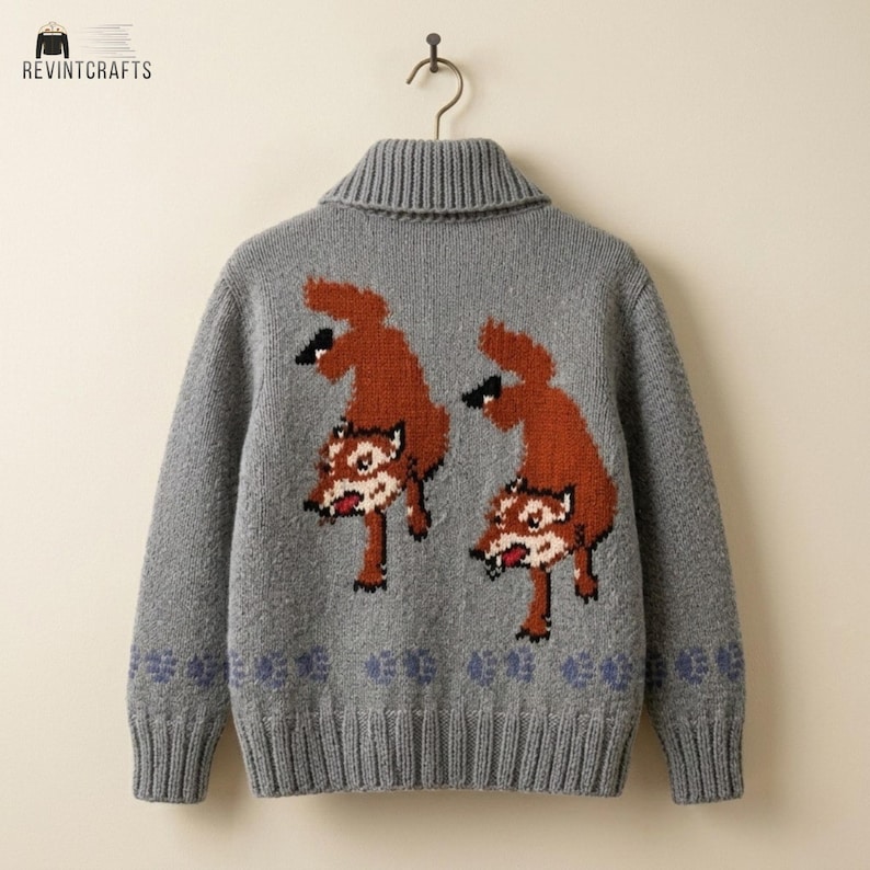 May include: A grey knit cardigan featuring a shawl collar and long sleeves. The back displays two brown fox motifs with white accents and a row of small blue paw prints along the bottom hem. The garment is displayed on a hanger against a plain background.