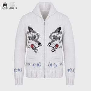 May include: A white zip-up knit cardigan featuring a shawl collar and long sleeves. The front displays two symmetrical wolf head motifs in gray, black, and red, with small blue paw print patterns near the ribbed hem and sleeve cuffs.