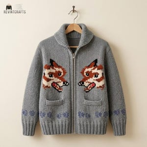 May include: A grey knit zip-up cardigan featuring a shawl collar, two front pockets, and a repeating pattern of fox faces on the chest with paw prints along the bottom hem. The garment is displayed on a wooden hanger against a plain background.