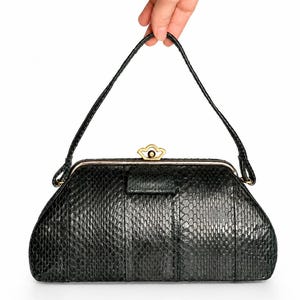 Peut inclure: Un sac à main vert foncé avec un motif texturé en peau de serpent, doté d'une poignée supérieure unique et d'une fermeture à cadre en métal doré. Le fermoir présente une forme festonnée décorative et le sac a une silhouette structurée.