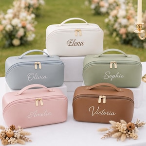 May include: Five rectangular cosmetic bags with top handles and gold-tone double zippers. The bags are white, light blue, sage green, light pink, and brown. Each bag features a custom name embroidered in white script: Elena, Olivia, Sophie, Amelia, and Victoria.