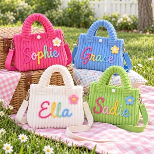 May include: Four small corduroy handbags in pink, blue, white, and green, each featuring a white snap closure, a matching shoulder strap, a small crocheted flower, and a personalised name in colourful, multi-toned script lettering.